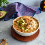bowl full of creamy, brothy soup piled with lots of texture in the center composed of crunchy tortilla strips, avocado, shredded chicken and finely diced, stewed tomatoes