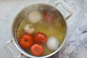 spaghetti noodles cooking in the bottom of a stockpot full of water with tomatoes, onions, garlic 