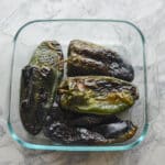 Roasted poblano peppers steaming inside a clear glass container