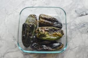Roasted poblano peppers steaming inside a clear glass container