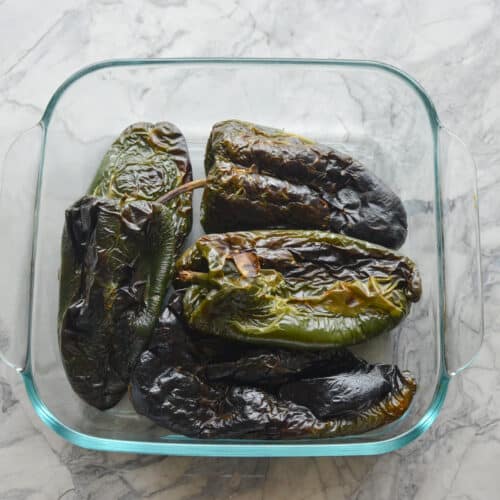 Roasted poblano peppers steaming inside a clear glass container