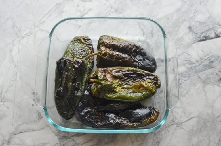 Roasted poblano peppers steaming inside a clear glass container