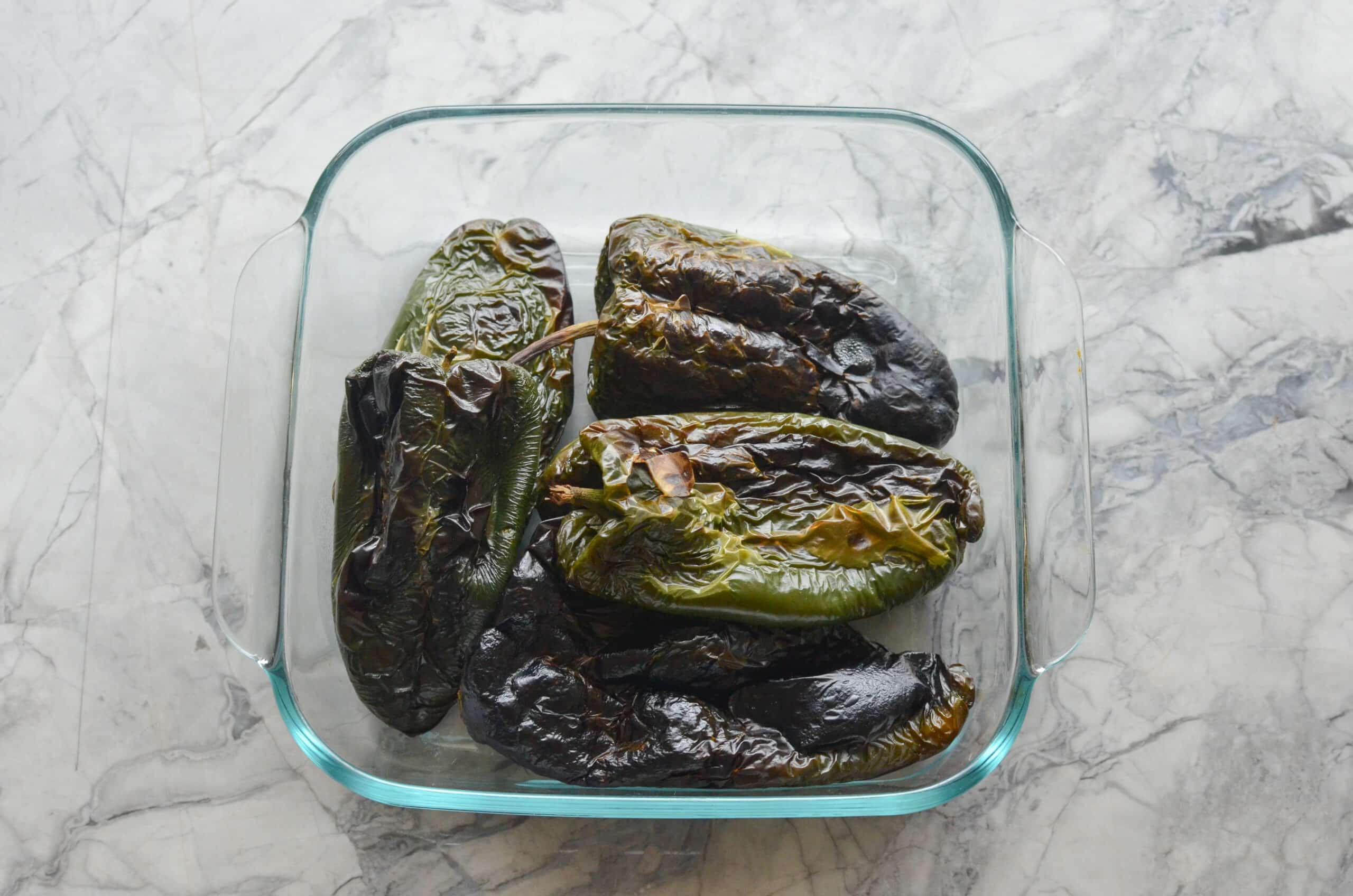 Roasted poblano peppers steaming inside a clear glass container