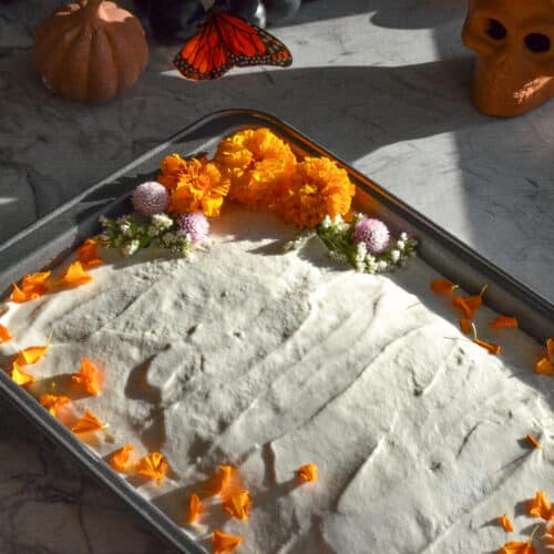 Pumpkin spice tres leches cake frosted with whipped cream and decorated with orange marigold flowers.