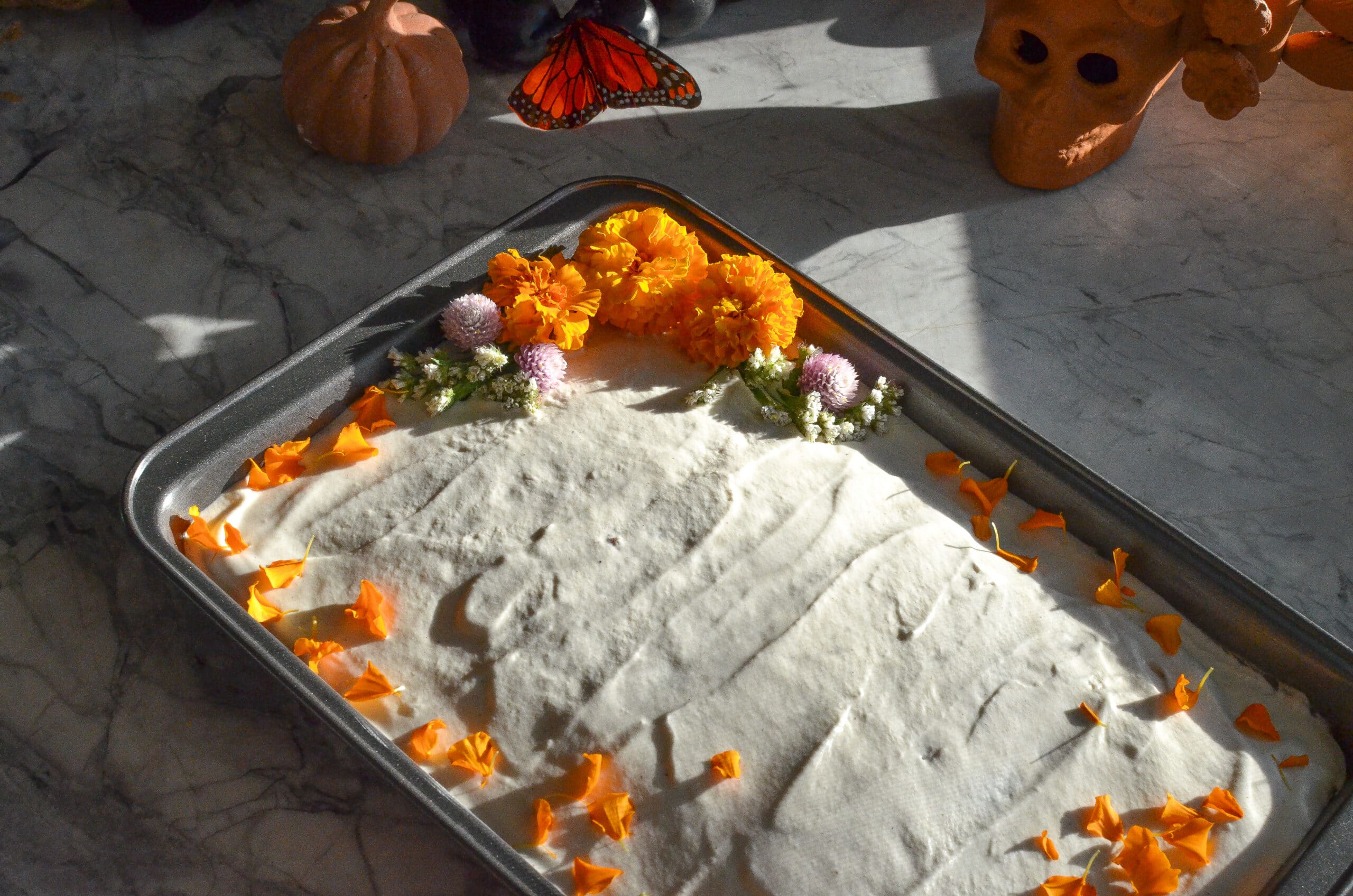 Pumpkin spice tres leches cake frosted with whipped cream and decorated with orange marigold flowers.