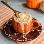 Creamy fall rice pudding overflowing an orange mug with a wooden spoon, styled with mini pumpkins.