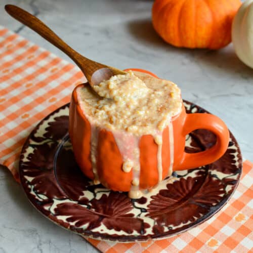 Creamy fall rice pudding overflowing an orange mug with a wooden spoon, styled with mini pumpkins.