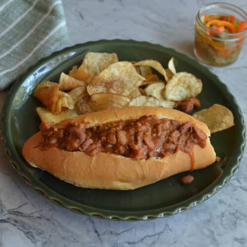 A completed Monterrey-style chili dog served on a plate with a side of crispy potato chips.