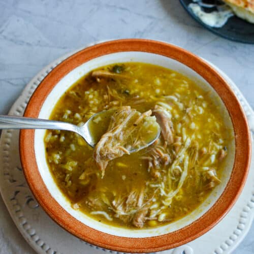 A spoon lifting tender shredded pork from a bowl of green chile stew topped with melted cheese.
